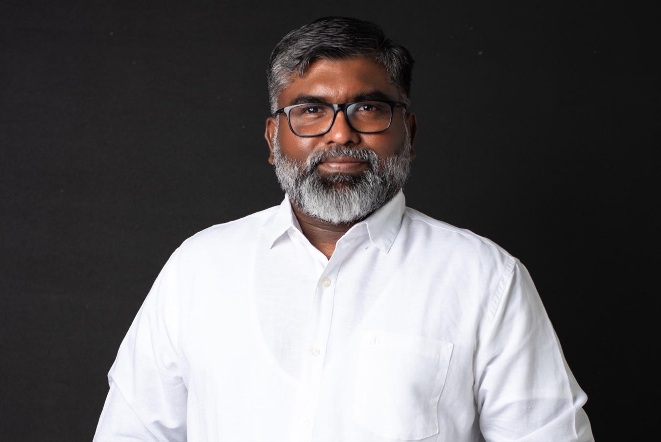 Lakmal Sameera De Silva in a white shirt against a dark backdrop